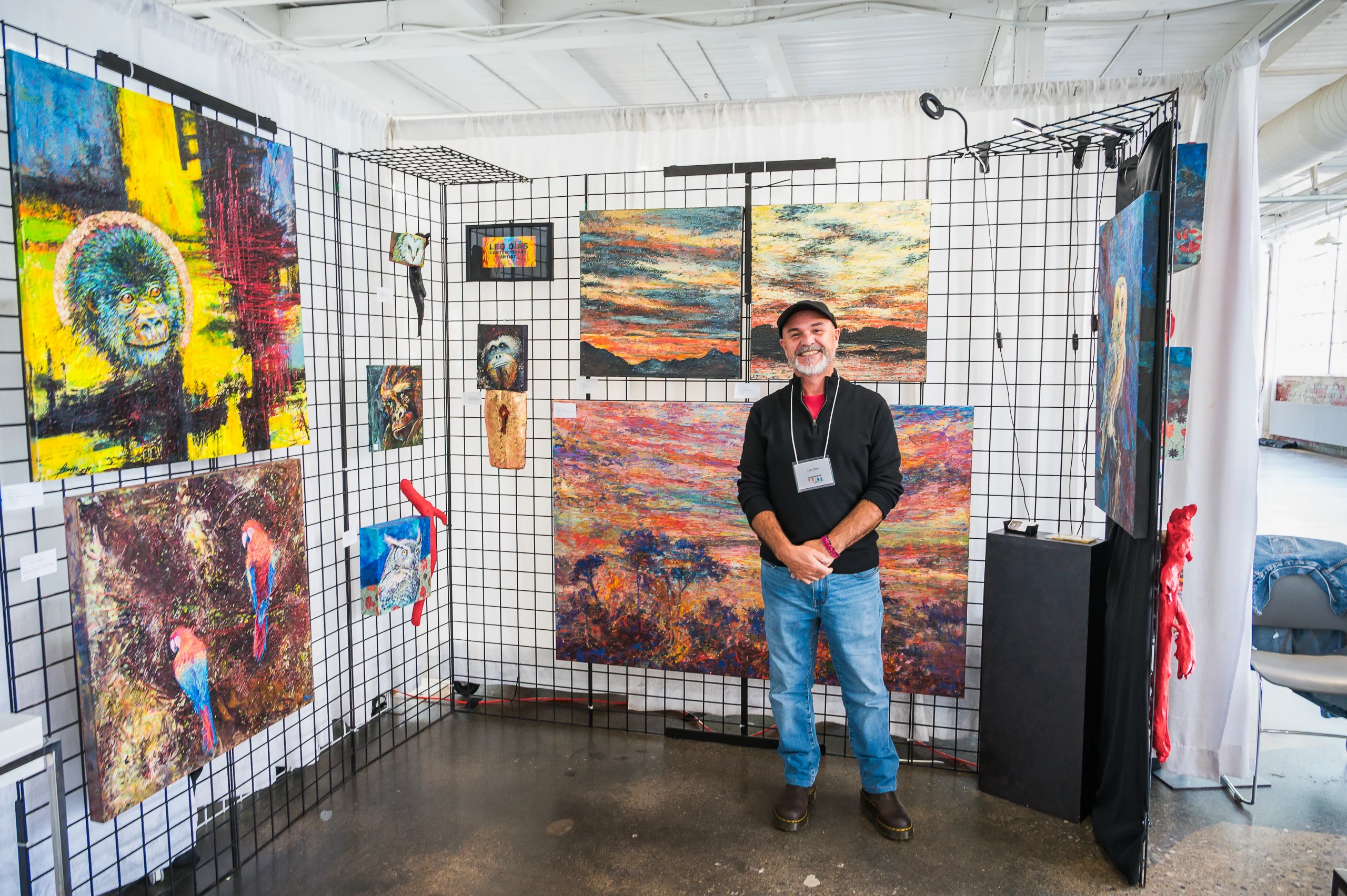 Leo Dias standing in his booth at an art show surrounded by his artwork.